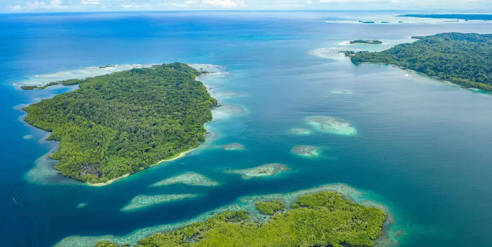 Forested islands and turquoise reef lagoons in Milne Bay, Papua New Guinea