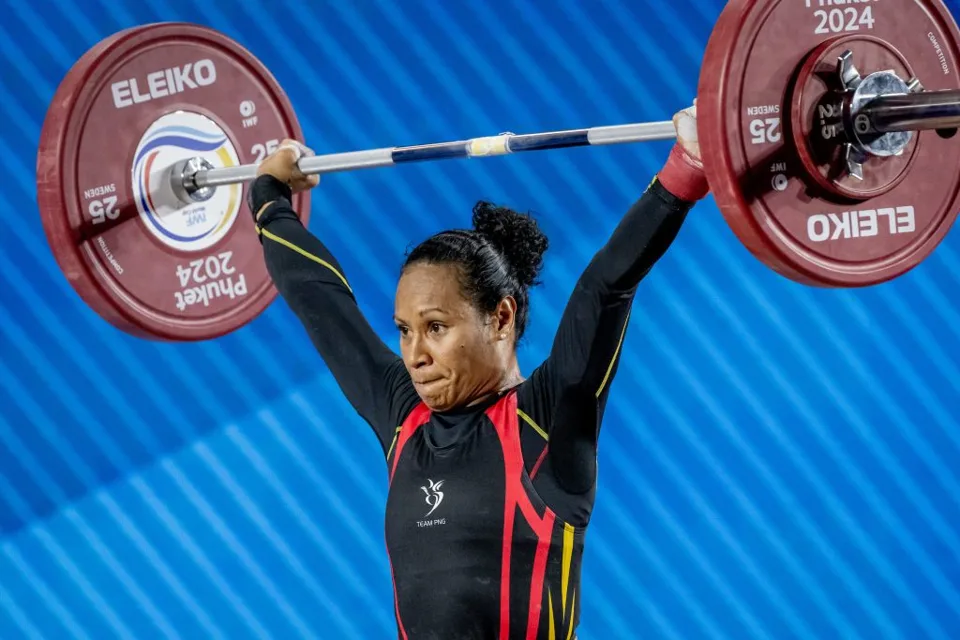 Dika Toua holding a loaded barbell overhead in competition
